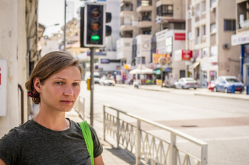 A young woman with a bag is standing at a crossroads at a traffic light