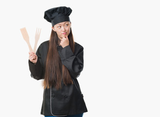 Young Chinese woman over isolated background wearing chef uniform serious face thinking about question, very confused idea