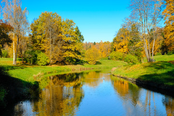 Beautiful autumn sunny landscape in Pavlovsk park with the Slavyanka river and trees with red and orange leaves, Pavlovsk, St. Petersburg.