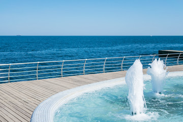 The gush of water of fountain. Splash and Foam of water. Blue vertical fountain with mosaic pool on the wooden terrace, by the sea. Rest on the beach, sea freshness in the summer heat. 