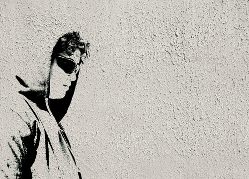 Sad troubled teenager school boy with hood posing alone. Image made like graffiti stencil painting on white textured concrete wall with copy space for writing - stock image