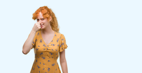 Young redhead woman smelling something stinky and disgusting, intolerable smell, holding breath with fingers on nose. Bad smells concept.