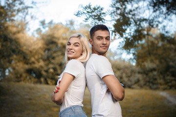 Obraz premium Cute loving couple standing back together on grass in nature green park with beautiful sundown light. Looking camera.