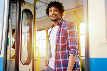 Young beautiful Afro-American man standing on door of public transport. Looking away and going out.