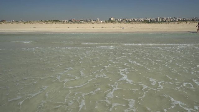 Clear skies and water, while standing in the ocean, perpendicular to sandy beach