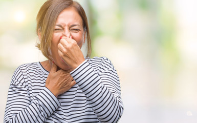 Middle age senior hispanic woman over isolated background smelling something stinky and disgusting, intolerable smell, holding breath with fingers on nose. Bad smells concept.