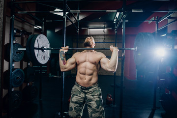 Fototapeta na wymiar Bearded guy with six-pack lifting barbell in crossfit gym. Weight plates in background.