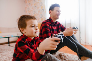 Happy father and son sitting on a floor and playing video games. Both of them very excited and focused.
