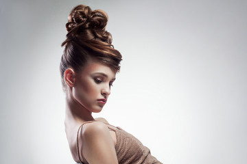 side view of attractive brunette woman with stylish hairdo and makeup posing on isolated grey background. indoor, studio shot on copy space.
