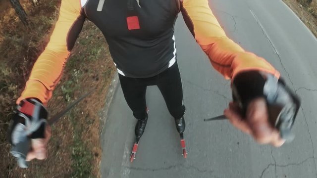 Training an athlete on the roller skaters. Biathlon ride on the roller skis with ski poles, in the helmet. Autumn workout. Roller sport. Adult man riding on skates. Pov view action cam. Slow motion.