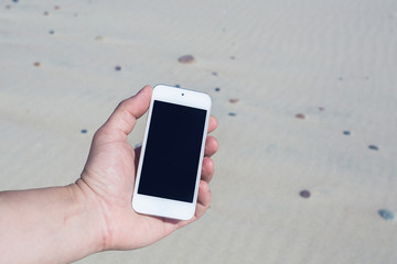 Hand holds smart phone, on beach background
