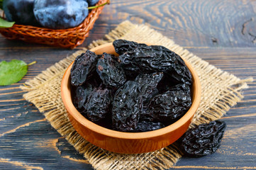 Prunes in a clay bowl and fresh plums, leaves on a wooden table. Fresh prunes for healthy life.