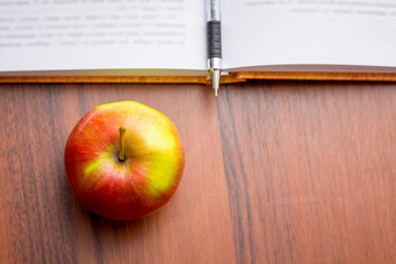 Ripe juicy red apple near the book and pen. Useful food during a break between work_