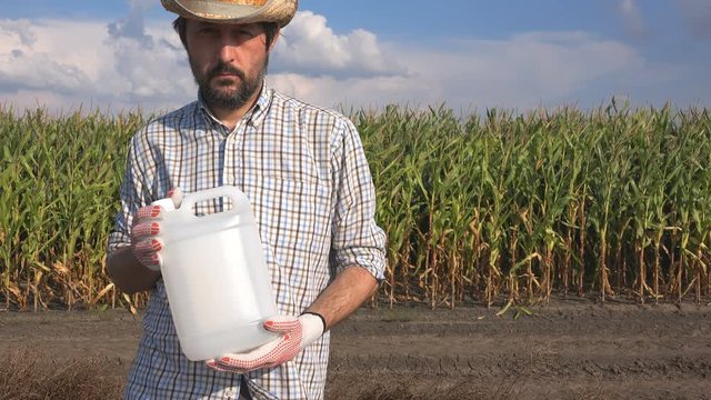 Farmer holding pesticide chemical jug in cornfield. Blank unlabeled bottle as mock up copy space for herbicide, fungicide or insecticide used in corn crop farming.