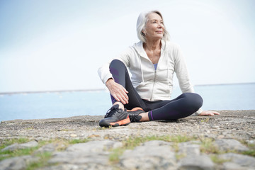  Beautiful elderly woman sitting by the ocean in sportswear