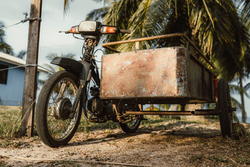 altes Motorrad auf Palmenstrand bei Sonnenuntergang