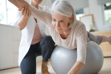 Senior woman exercising with her physiotherapist and swiss ball - obrazy, fototapety, plakaty