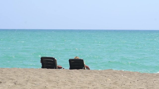 Young Couple Lying On A Lounge Chair On The Beach Watching