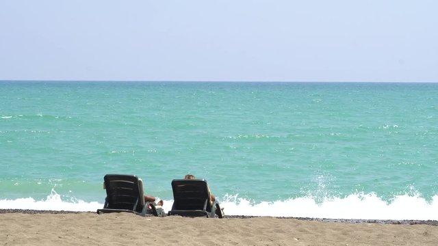 Young Couple Lying On A Lounge Chair On The Beach Watching