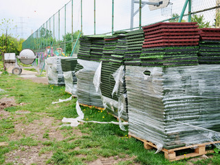 Stack of rubber floor tile mats and artificial turf grass rug tiles for elastic safety flooring. Low cost solution safety surfacing mats for playgrounds, sport fields and recreational facilities.
