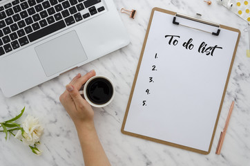 Office work flat lay. Girl writing to-do list in clip board. Computer, supplies, cup of coffee and...