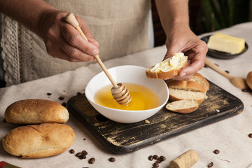 Women's hands putting honey from white bowl on sandwich with butter by honey stick