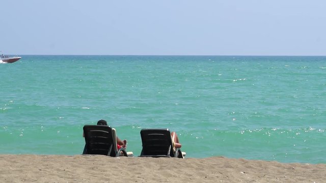 Young Couple Lying On A Lounge Chair On The Beach Watching
