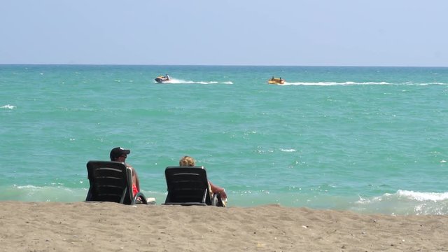 Young Couple Lying On A Lounge Chair On The Beach Watching