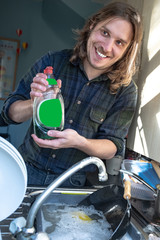 Fototapeta na wymiar Young man with long hair and beard posing with bottle while doing the dishes
