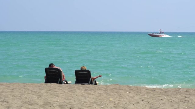 Young Couple Lying On A Lounge Chair On The Beach Watching