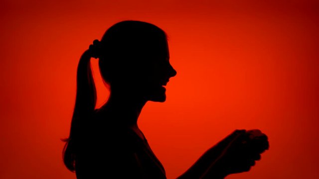 Silhouette of young woman gamer playing video game online. Female's face in profile with game console on red background. Black contour shadow of teenager's half-face winning computer game