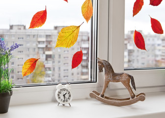 Bright autumn leaves on the window glass, toy horse and clock on the windowsill