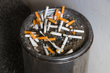 The cigarette butts in ashtray with sand at smoking.