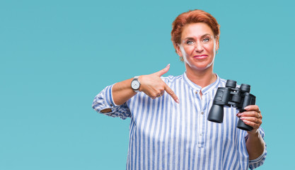 Fototapeta na wymiar Senior caucasian woman looking through binoculars over isolated background with surprise face pointing finger to himself