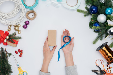 partial view of woman holding blue ribbon and wrapped christmas gift in hands isolated on white