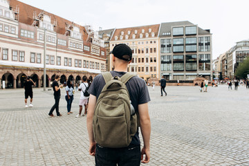 Tourist man with backpack or student in Leipzig Square in Germany admiring beautiful buildings or...