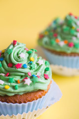 Closeup two New Year cupcakes with creamy green top with colorful stars and sprinkles on yellow background.
