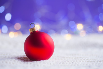 Red Christmas ball on white knitted fabric on purple background with warm bokeh