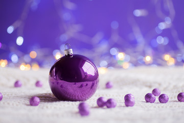 Purple Christmas ball and beads on white knitted fabric on purple background with warm bokeh.