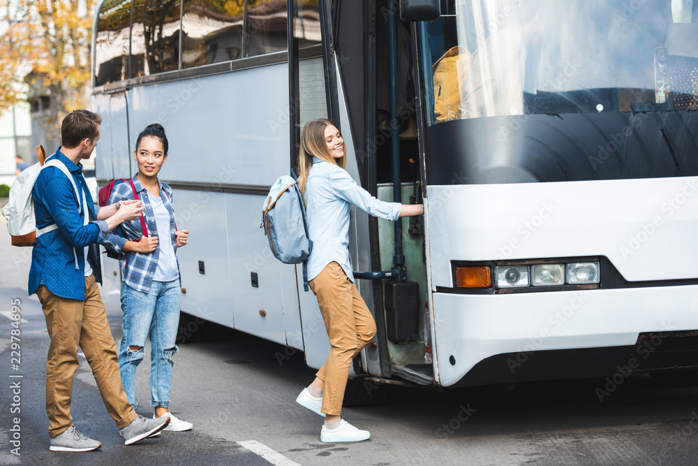 Wall mural selective focus of multiethnic tourists with backpacks walking into travel bus at city street