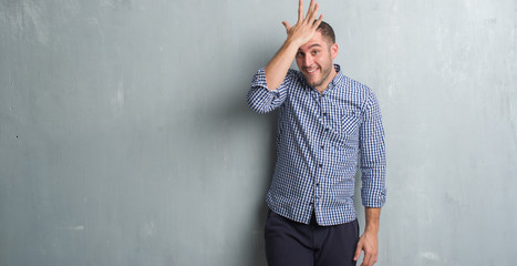 Young caucasian man over grey grunge wall surprised with hand on head for mistake, remember error....