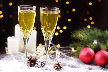 Two glasses of champagne or juice on the table, decorated with a glowing garland, red balls, a Christmas tree branch and white candles