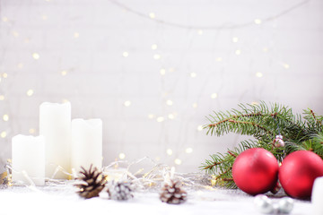 White background for a Christmas card, a wall with glowing garland, red Christmas balls and white candles on the table