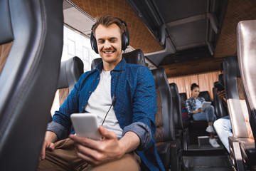 Fototapeta na wymiar happy adult man in headphones listening music and using smartphone during trip on bus