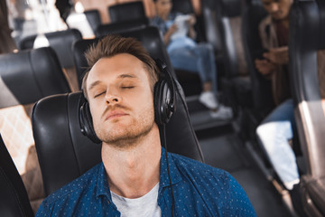 handsome male tourist  in headphones listening music and sleeping during trip on bus