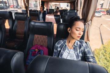 asian young woman sleeping and listening music in earphones during trip on travel bus
