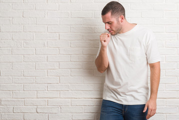 Young caucasian man standing over white brick wall feeling unwell and coughing as symptom for cold or bronchitis. Healthcare concept.