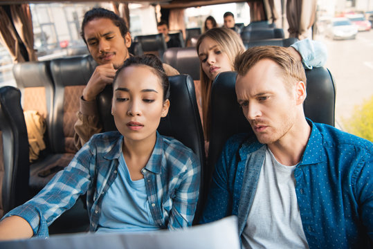 pensive multiethnic tourists looking at map during trip on travel bus