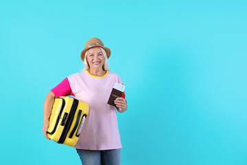 Senior woman with suitcase and passport on color background. Space for text