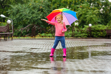 Cute little girl with bright umbrella under rain on street